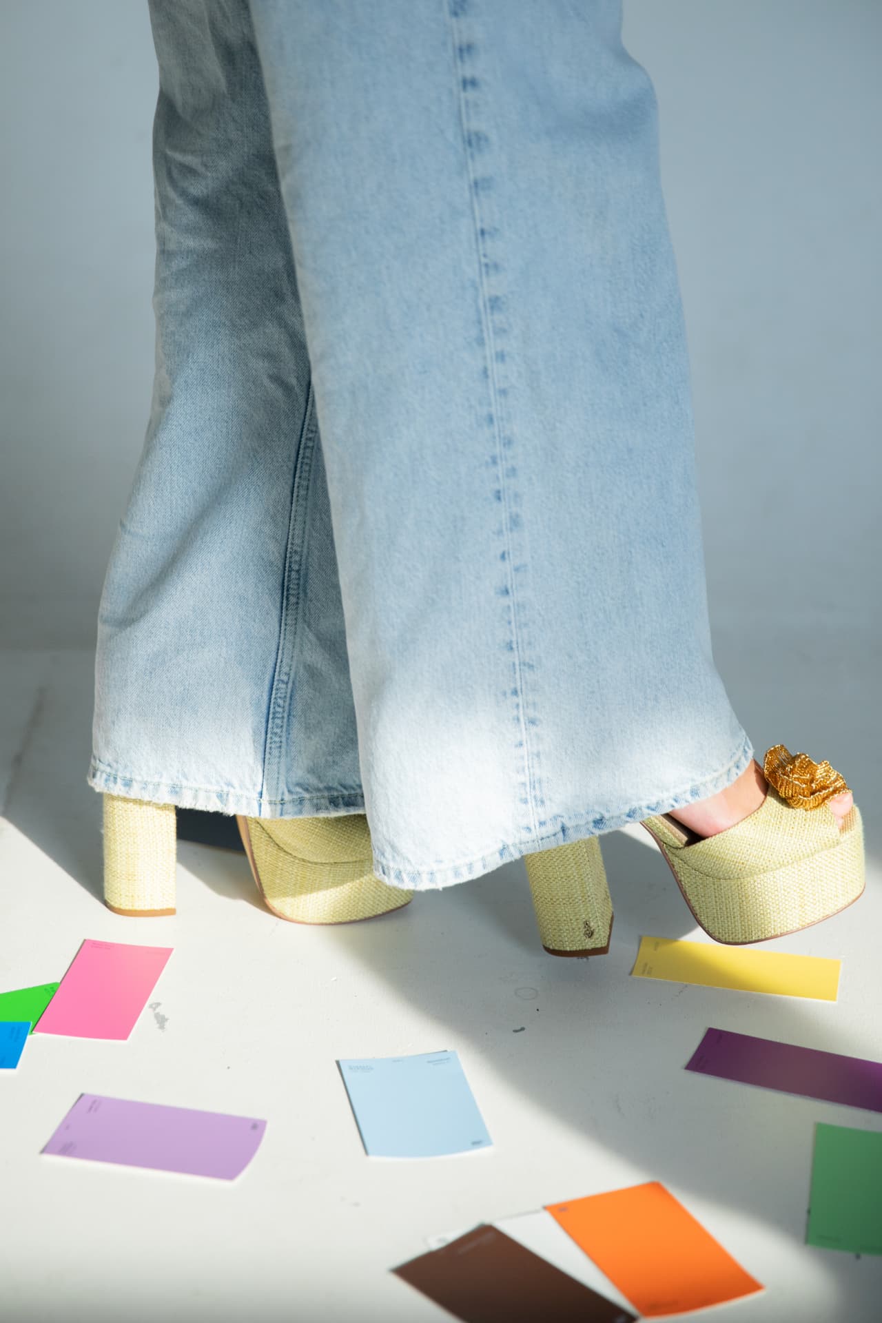 Wide-leg denim and raffia platforms among scattered paint swatches