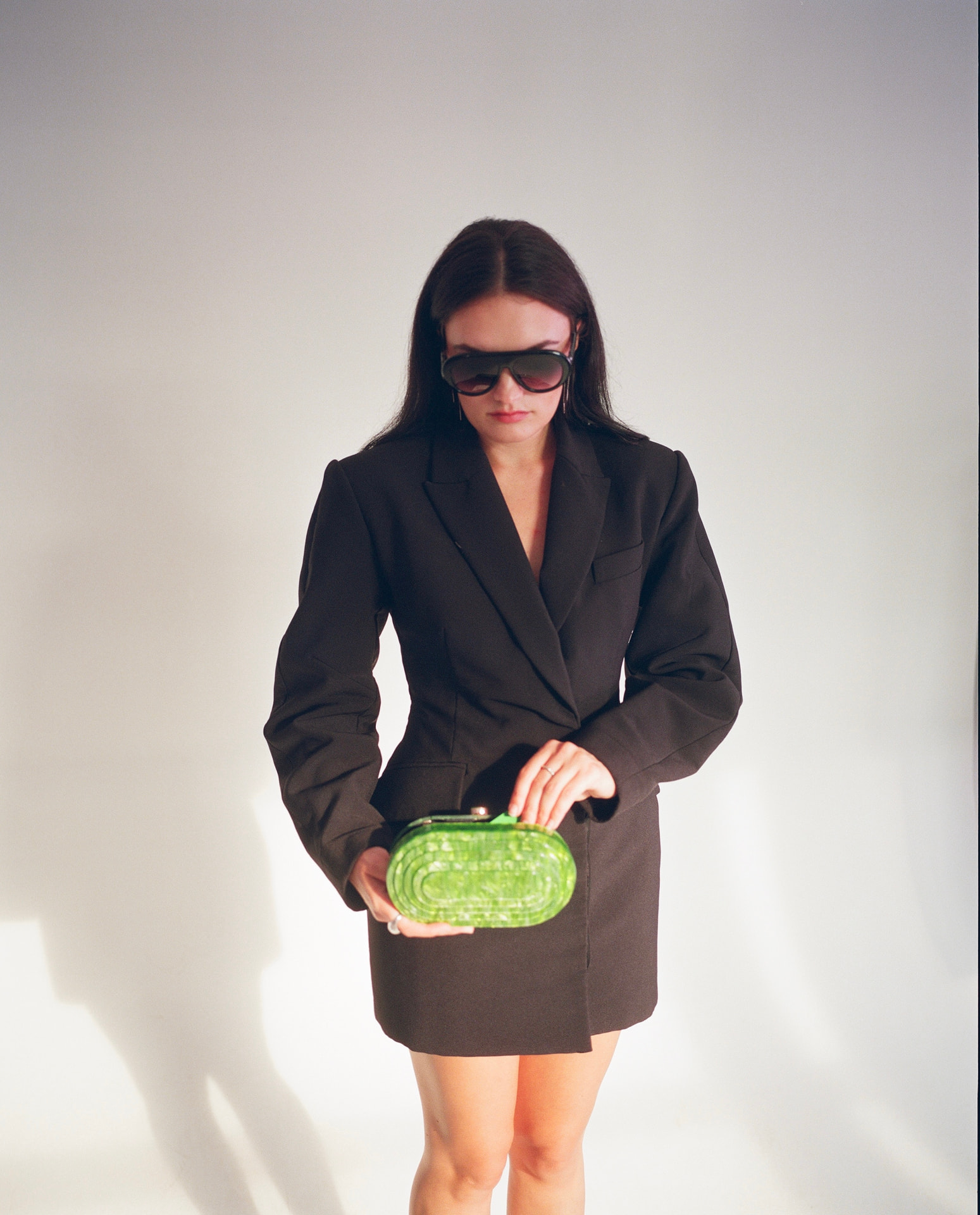 Full-length portrait in a tailored blazer dress with green clutch